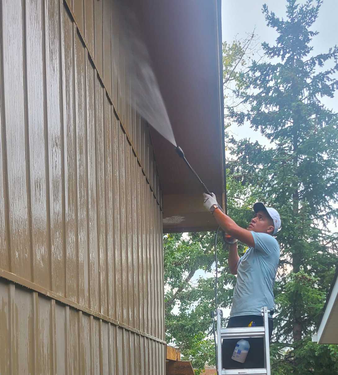 Pro Window Cleaning Calgary technician on a ladder pressure washing the soffit of a Calgary home