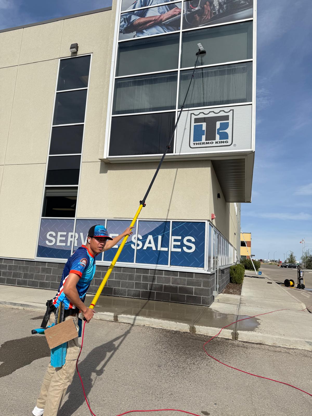 Pro Window Cleaning Calgary technician using a water-fed pole to clean upper-level windows on a commercial building in Calgary