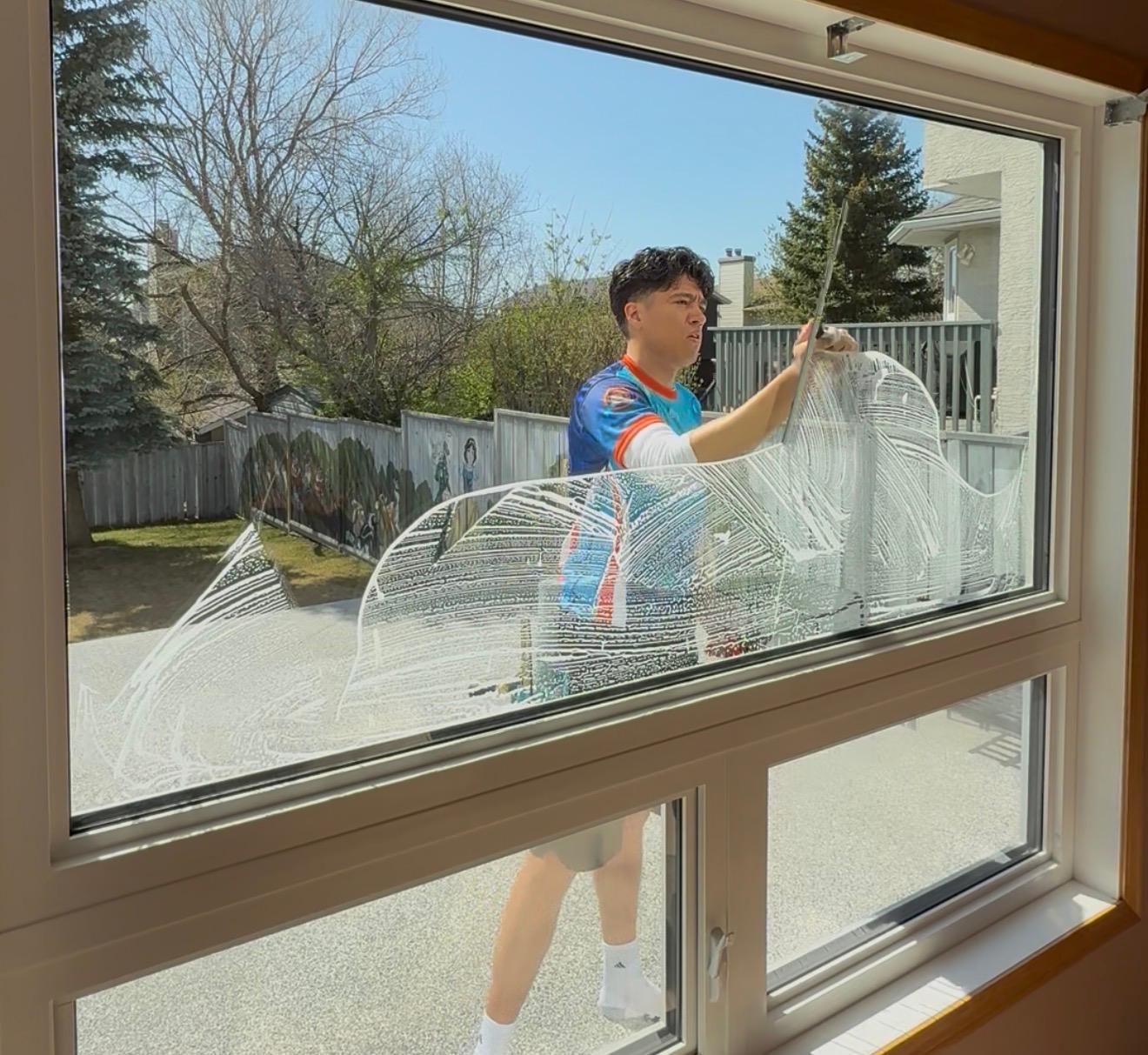 Pro Window Cleaning Calgary technician scrubbing the exterior of a residential window with a washer on a sunny Calgary day