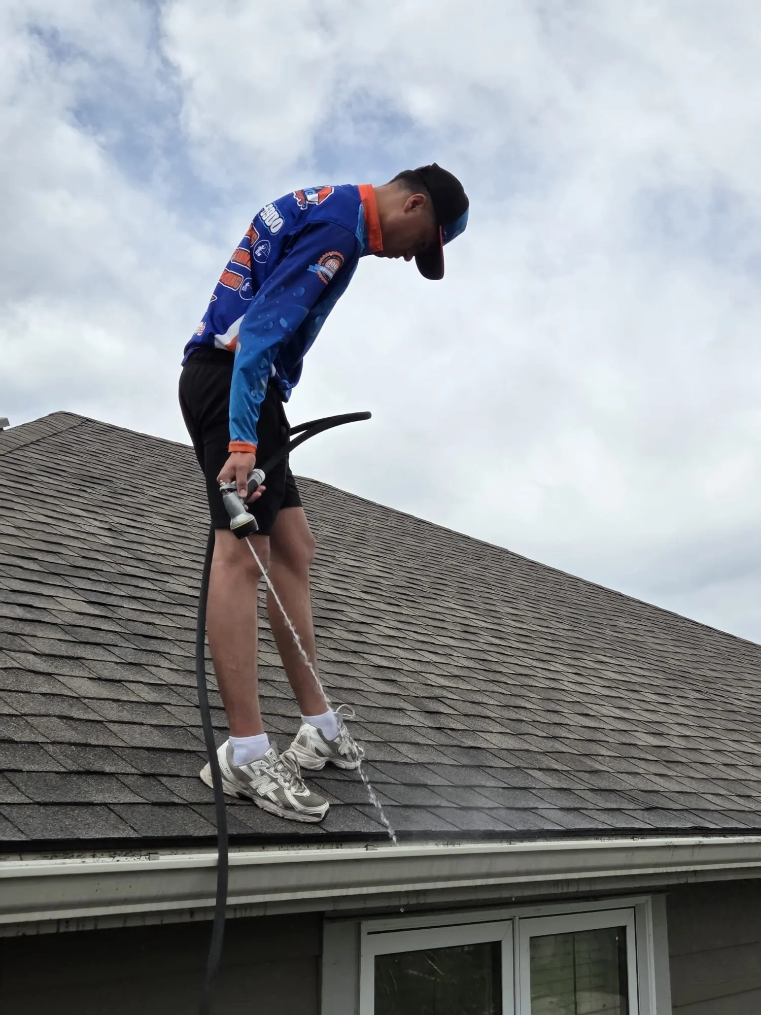 Calgary gutter cleaning technician flushing gutters with a hose on a residential rooftop