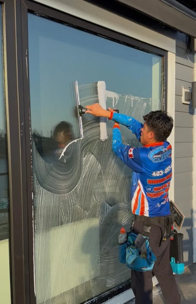 Pro Window Cleaning Calgary technician scrubbing and squeegeeing a large exterior glass panel on a Calgary home